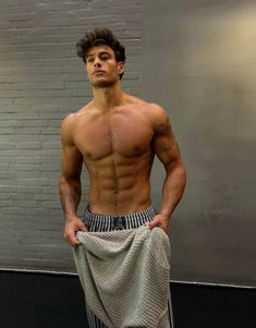 a shirtless man standing in front of a brick wall with his hands on his hips