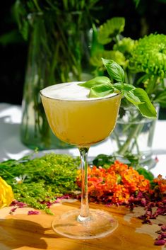 a glass filled with a drink sitting on top of a wooden table next to flowers