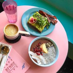 a pink table topped with two plates of food and cups of coffee next to each other