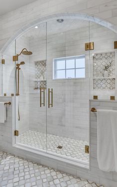 a bathroom with white tile and gold accents on the shower door, windows, and towels