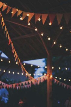 the lights are hanging from the roof above the tables at this outdoor wedding reception, which is decorated with bunting and paper garlands