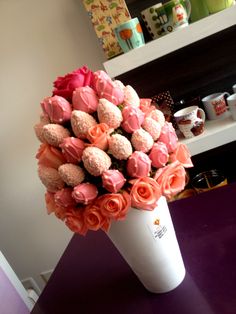 a white vase filled with pink and orange flowers on top of a purple countertop