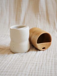 a white vase sitting on top of a bed next to a wooden tube shaped container