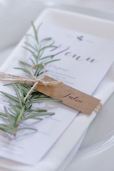 a place setting with an evergreen branch tied around the place card and twine of twine