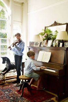 two young boys playing music in front of a piano and dog sitting on the floor