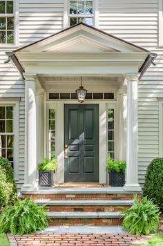 the front door of a house with brick steps and potted plants on either side