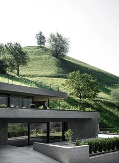 a modern house on the side of a hill with trees and bushes growing out of it