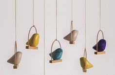 four different colored birds hanging from hooks on the wall in front of a white wall