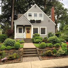 a gray house with yellow door and steps leading up to the front entrance, surrounded by trees