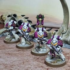 some white and purple painted warhammers on a table with skulls in the background