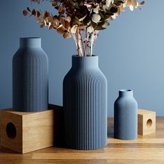 three blue vases sitting next to each other on top of a wooden table with flowers in them