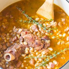 a pot filled with beans and meat next to a wooden spoon