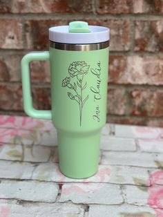 a green coffee cup with a flower on the side sitting on top of a brick wall