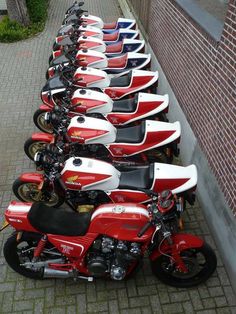 a row of motorcycles parked next to each other on the side of a road in front of a brick wall