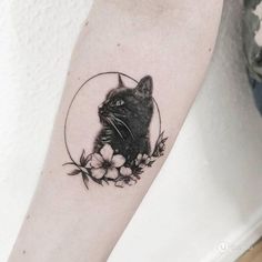 a black cat sitting in a circle with flowers on it's arm and behind its ear