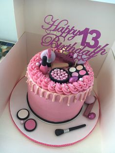 a birthday cake with pink icing and makeup on top, in a white box