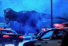 an image of a dinosaur on the street with police cars in front of it at night