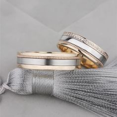 two gold and silver wedding bands with diamonds on the side, next to a tassel