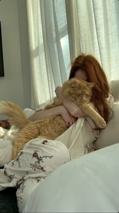 a woman laying on top of a bed holding a cat