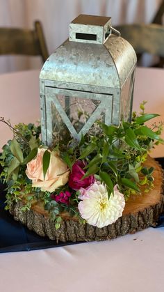 a table topped with a metal lantern and flowers on top of a piece of wood