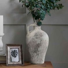 a white vase sitting on top of a wooden table next to a framed photo and potted plant