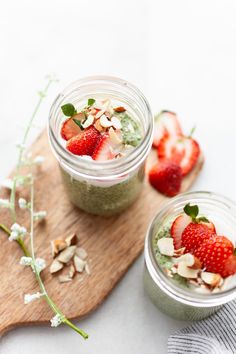 two mason jars filled with yogurt, strawberries and almonds on a cutting board