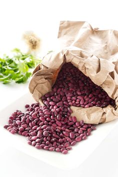 purple beans are in a paper bag on a white plate next to some green leaves