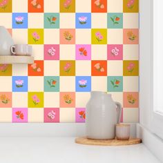 a vase and some cups on a counter in front of a wall with colorful squares