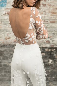 the back of a woman's dress with white flowers and leaves on it, in front of a brick wall