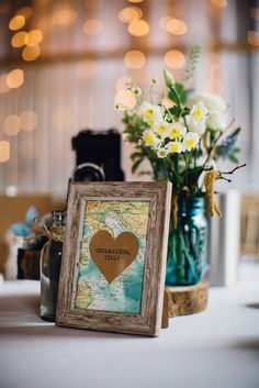 a table topped with a vase filled with white flowers and a framed heart on top of it