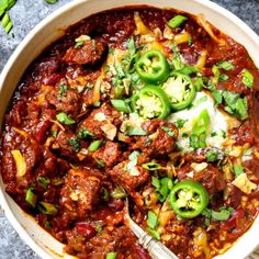 a white bowl filled with chili and meat covered in cheese, green peppers and sour cream