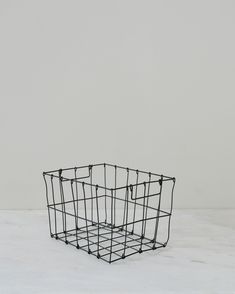 a black wire basket sitting on top of a white counter next to a gray wall