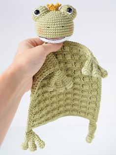 a hand holding a crocheted frog toy in it's left arm and the top part of its head