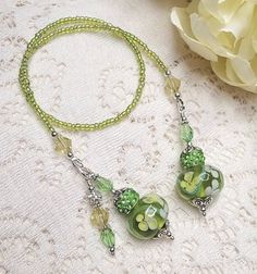 two green beads are attached to a necklace on a lace tablecloth with flowers in the background