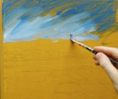 someone is painting on the wall with blue and yellow paint, while holding a brush in their left hand