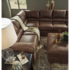 a living room with a large brown couch and ottoman next to a lamp on a table