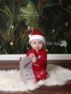 a baby is sitting on the floor with a christmas hat and holding a paper sign