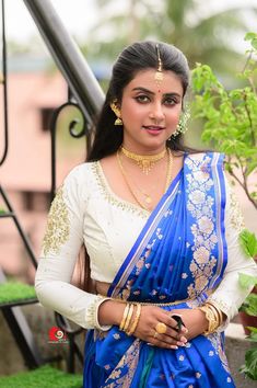 a woman in a blue and white sari with gold jewelry on her neck, posing for the camera