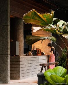 a woman standing in front of a counter next to a plant