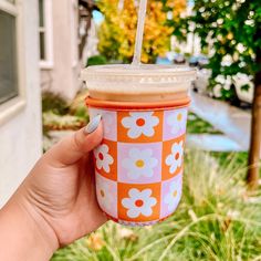 a person holding up a cup with a straw in it and flowers on the outside