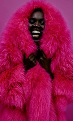 a woman wearing a pink fur coat and black makeup is posing in front of a purple background