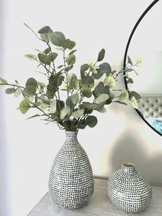 two vases with plants in them sitting on a table next to a round mirror