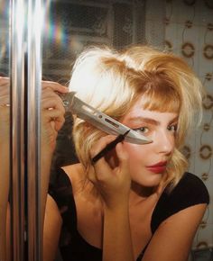 a woman holding a large pair of scissors in front of her face as she looks into the mirror