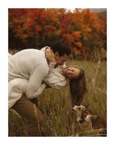 a man and woman are kissing in the grass with a dog behind them on a fall day