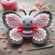 a crocheted butterfly sitting on top of a wooden table next to yarn and knitting needles