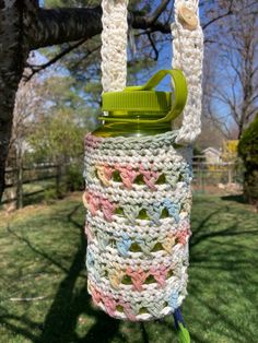 a crocheted bag hanging from a tree in the grass with a green handle