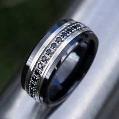 a black and white wedding ring with diamonds on it's side, sitting on top of a metal pole