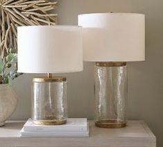 two clear glass lamps sitting on top of a white table next to a vase filled with flowers