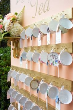 a wooden rack with cups and saucers hanging on it's sides next to a pink wall