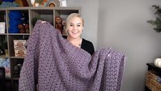 a woman holding up a purple crocheted blanket